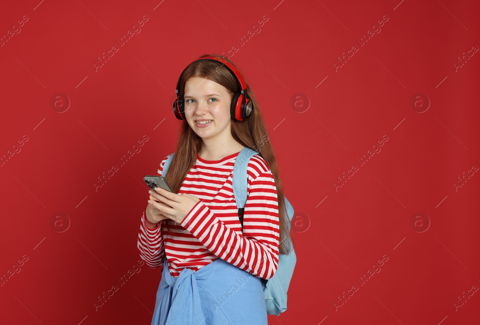 Teenage girl with smartphone listening to music on red background Photo of Teenage girl with smartphone listening to music on red background