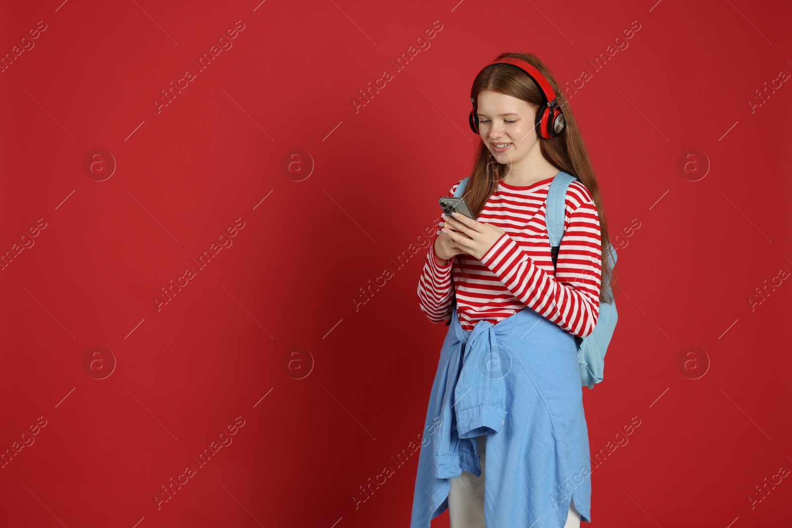 Teenage girl with smartphone listening to music on red background. Space for text Photo of Teenage girl with smartphone listening to music on red background. Space for text