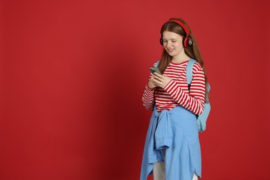 Photo of Teenage girl with smartphone listening to music on red background. Space for text