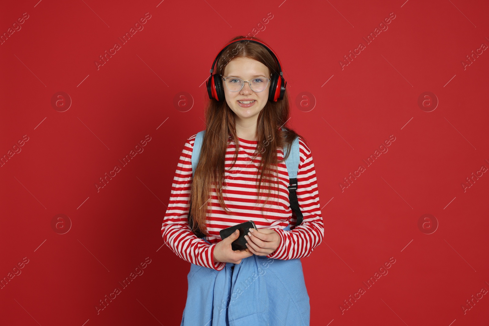 Teenage girl with smartphone listening to music on red background Photo of Teenage girl with smartphone listening to music on red background