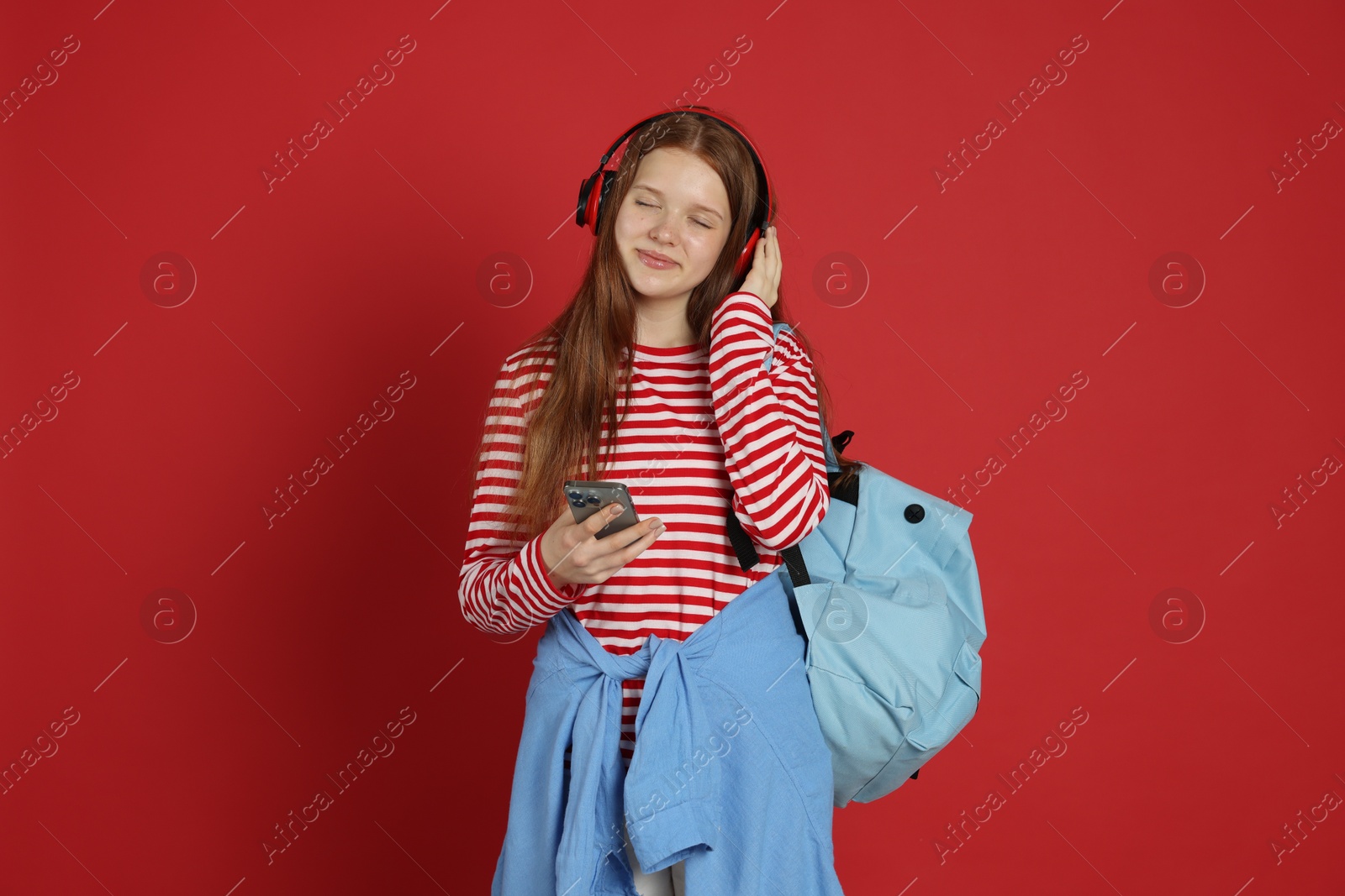 Teenage girl with smartphone listening to music on red background Photo of Teenage girl with smartphone listening to music on red background