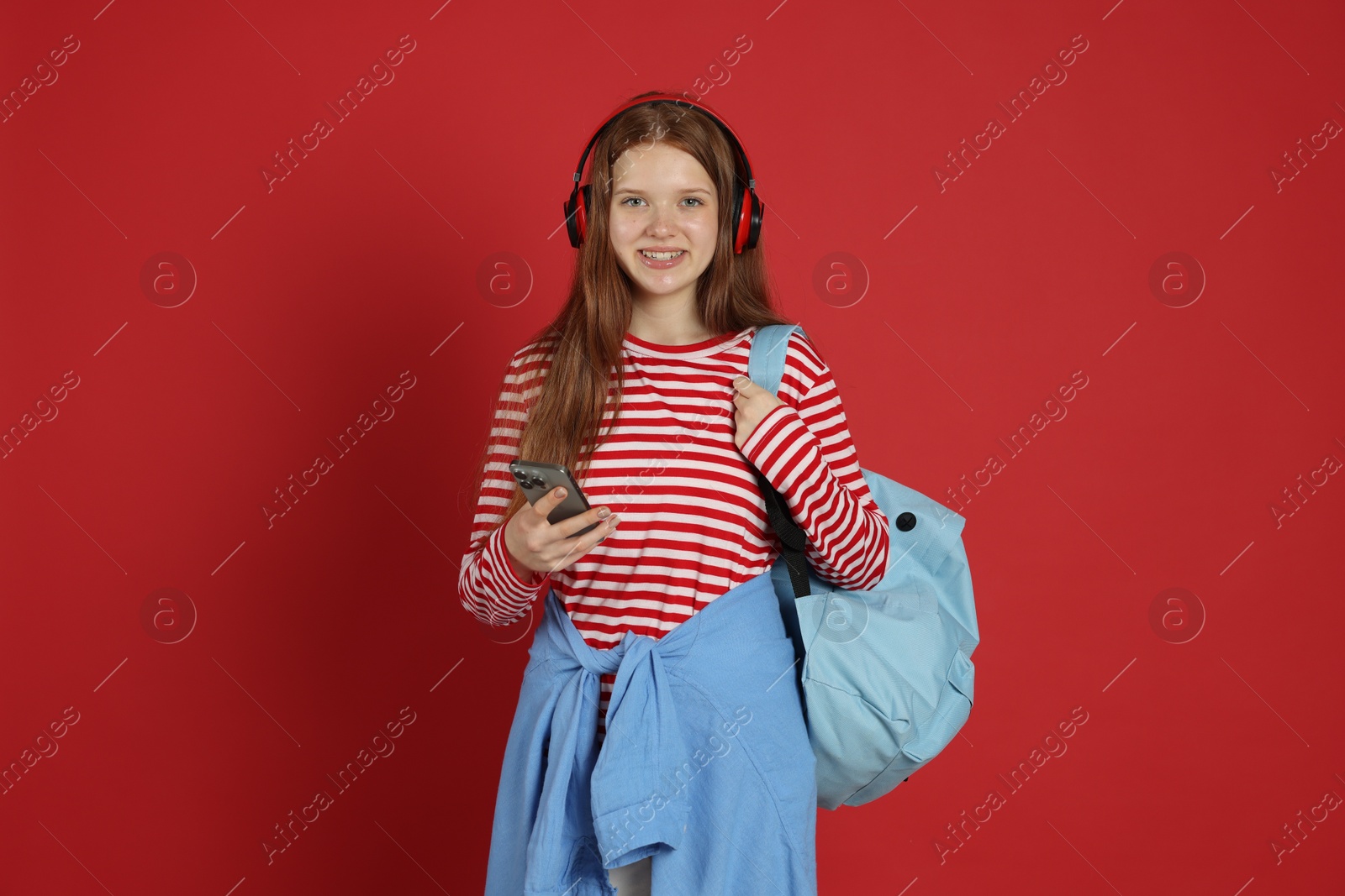 Teenage girl with smartphone listening to music on red background Photo of Teenage girl with smartphone listening to music on red background