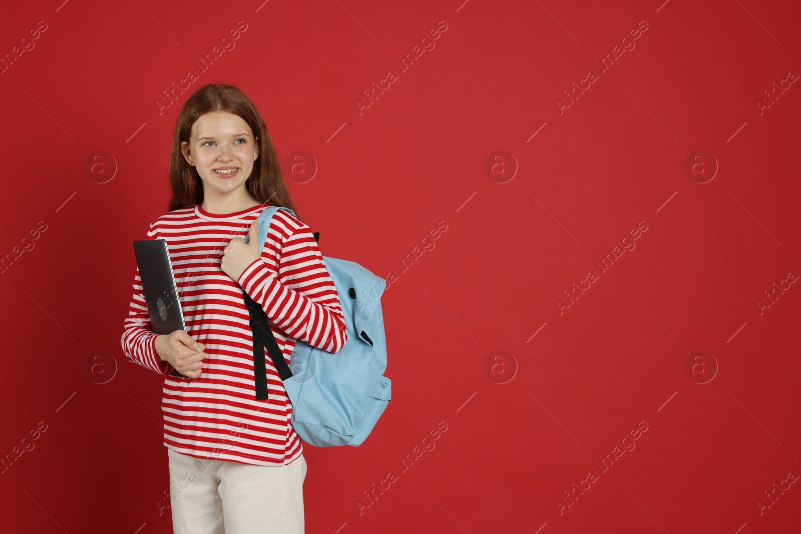 Teenage girl with backpack and laptop on red background. Space for text Photo of Teenage girl with backpack and laptop on red background. Space for text