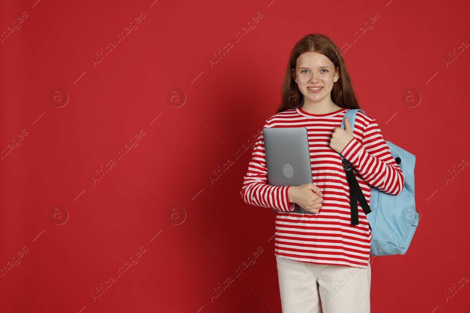Teenage girl with backpack and laptop on red background. Space for text Photo of Teenage girl with backpack and laptop on red background. Space for text