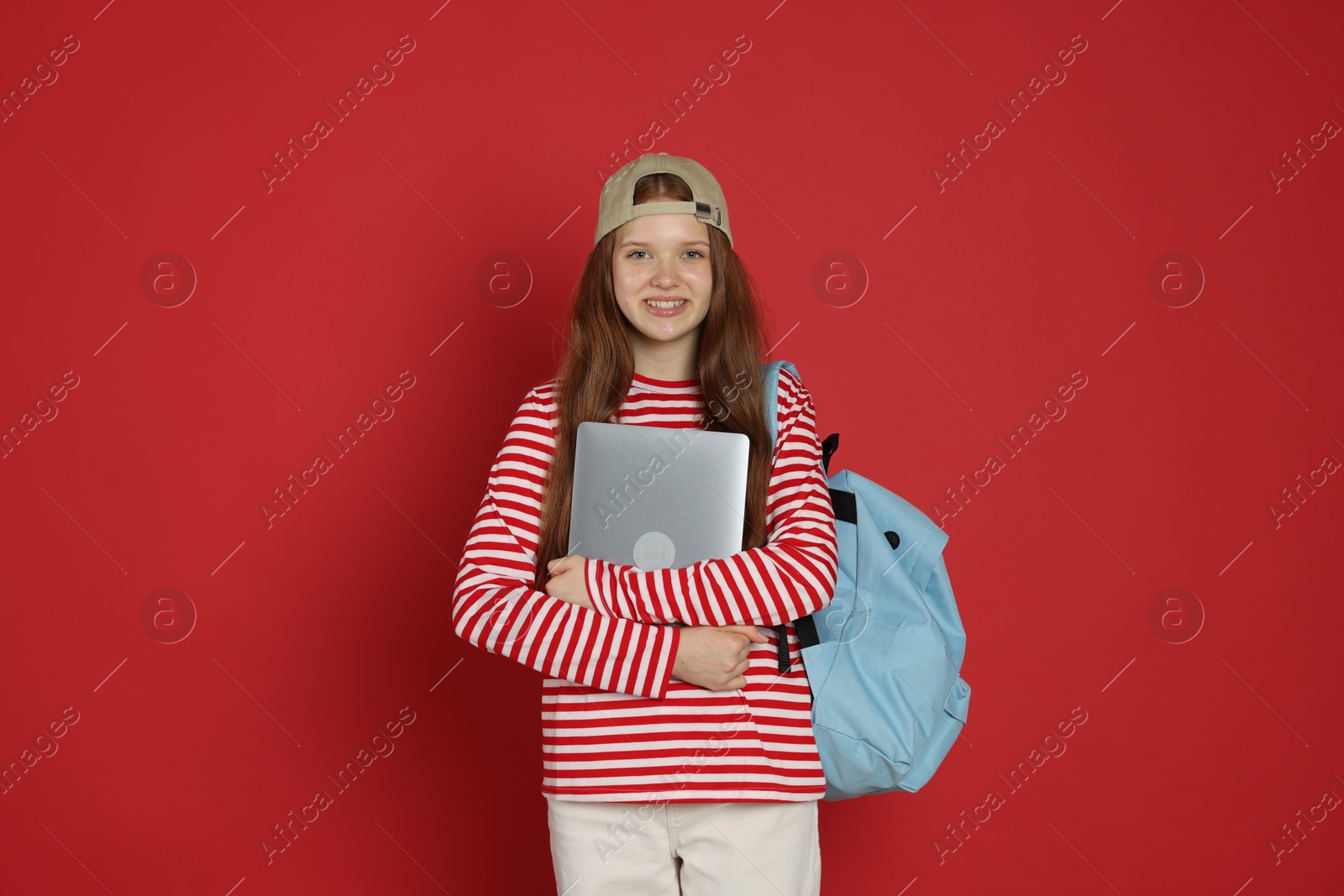 Teenage girl with backpack and laptop on red background Photo of Teenage girl with backpack and laptop on red background