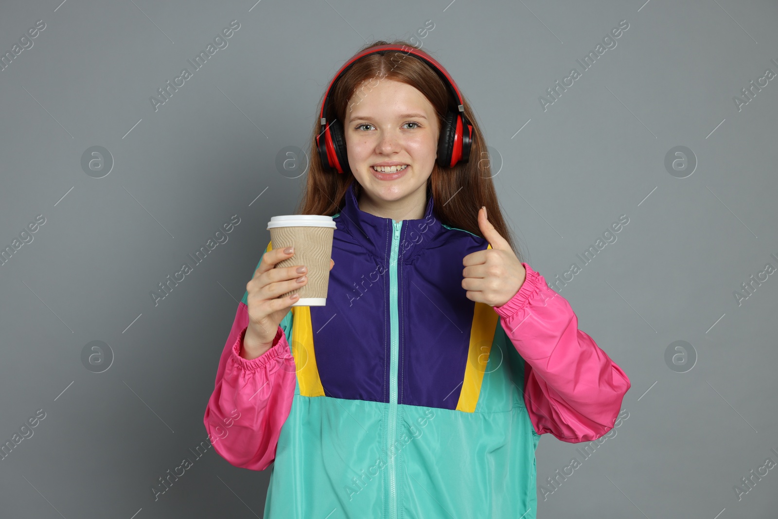 Photo of Teenage girl with drink showing thumbs up on grey background