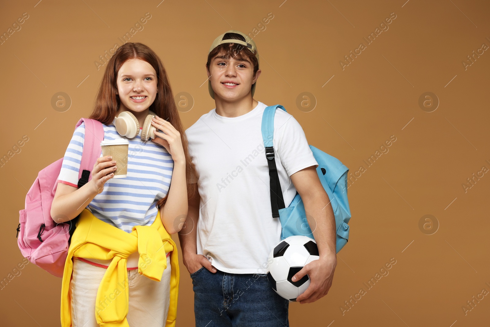Teenagers with backpacks, soccer ball and drink on brown background Photo of Teenagers with backpacks, soccer ball and drink on brown background