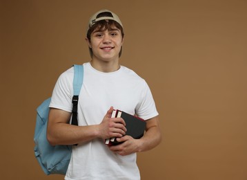 Photo of Teenage boy with backpack and books on brown background. Space for text