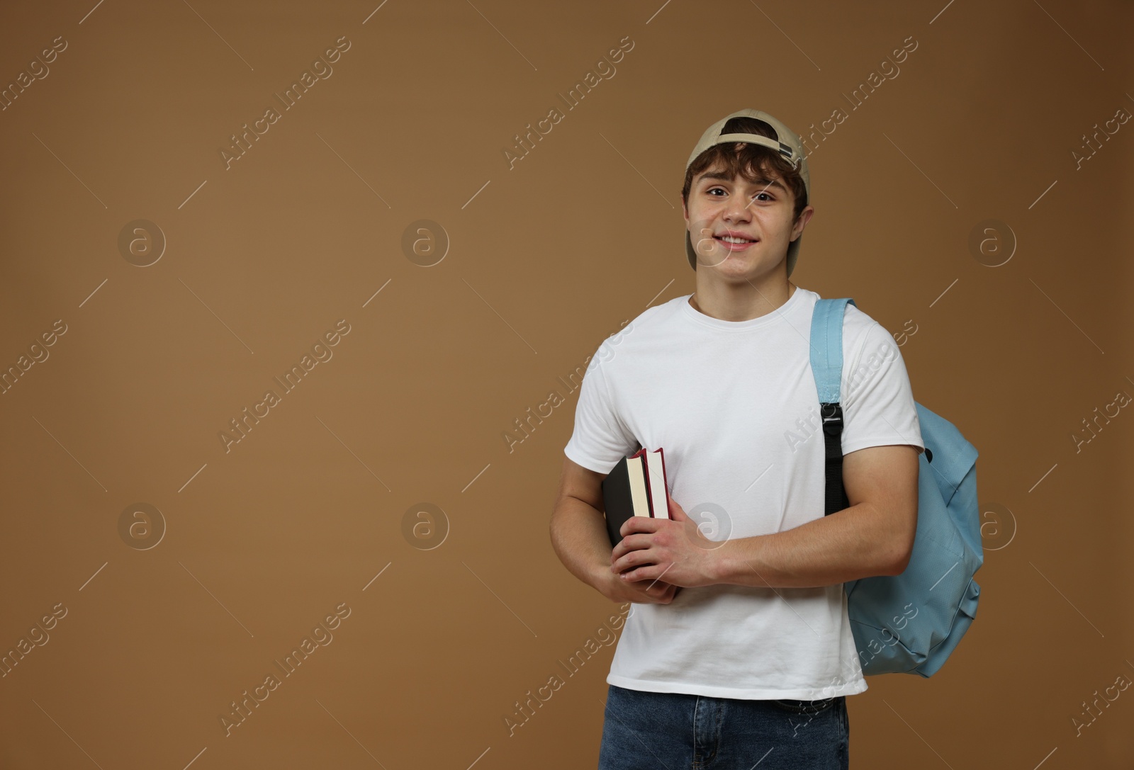 Teenage boy with backpack and books on brown background. Space for text Photo of Teenage boy with backpack and books on brown background. Space for text