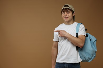 Photo of Teenage boy with backpack pointing at something on brown background. Space for text