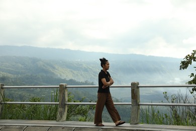 Photo of Bali, Indonesia - May 18, 2025: Woman walking across bridge against picturesque mountain view