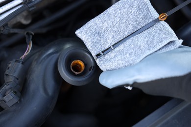 Photo of Worker checking motor oil level in car with dipstick, closeup