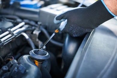 Photo of Worker checking motor oil level in car with dipstick, closeup