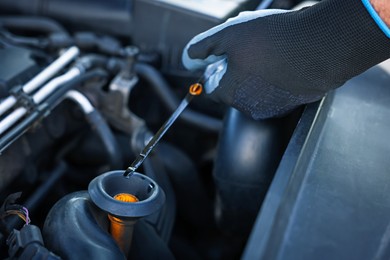 Photo of Worker checking motor oil level in car with dipstick, closeup