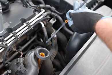Photo of Worker checking motor oil level in car with dipstick, closeup