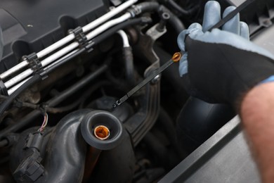 Photo of Worker checking motor oil level in car with dipstick, closeup