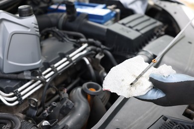 Photo of Worker checking motor oil level in car with dipstick, closeup