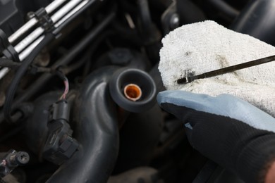 Photo of Worker checking motor oil level in car with dipstick, closeup