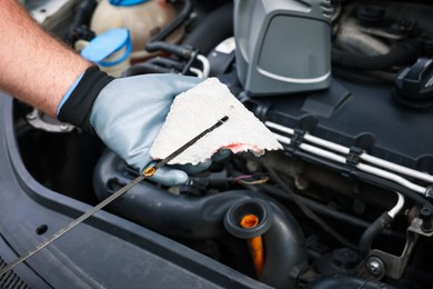 Photo of Worker checking motor oil level in car with dipstick, closeup