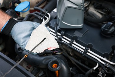 Photo of Worker checking motor oil level in car with dipstick, closeup