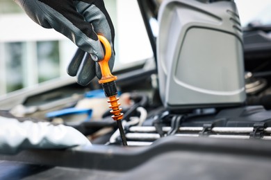 Photo of Worker checking motor oil level in car with dipstick, closeup