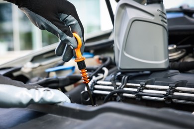 Photo of Worker checking motor oil level in car with dipstick, closeup