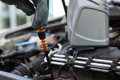 Photo of Worker checking motor oil level in car with dipstick, closeup