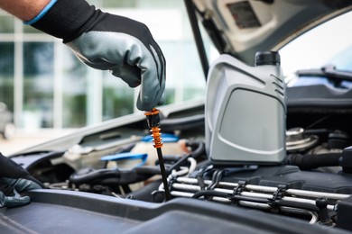 Photo of Worker checking motor oil level in car with dipstick, closeup