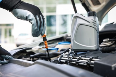 Photo of Worker checking motor oil level in car with dipstick, closeup