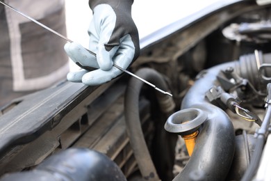Photo of Worker checking motor oil level in car with dipstick, closeup
