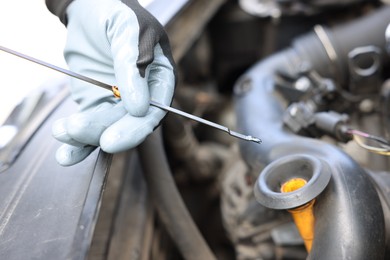 Photo of Worker checking motor oil level in car with dipstick, closeup