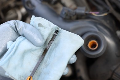 Photo of Worker checking motor oil level in car with dipstick, closeup