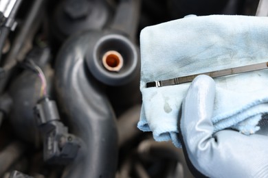 Photo of Worker checking motor oil level in car with dipstick, closeup