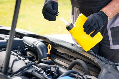 Photo of Worker checking motor oil level in car with dipstick, closeup