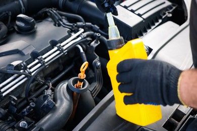 Photo of Worker checking motor oil level in car with dipstick, closeup