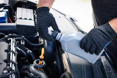 Photo of Worker checking motor oil level in car with dipstick, closeup