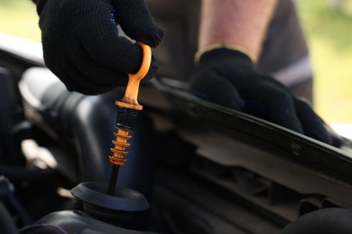 Photo of Worker checking motor oil level in car with dipstick, closeup
