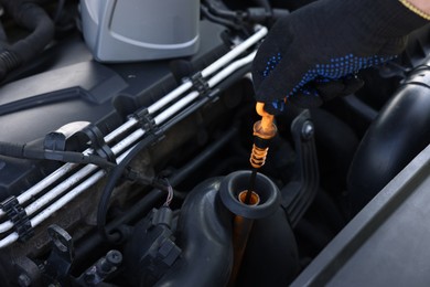 Photo of Worker checking motor oil level in car with dipstick, closeup