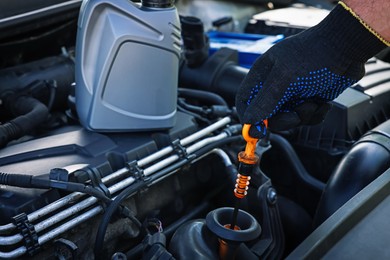 Photo of Worker checking motor oil level in car with dipstick, closeup