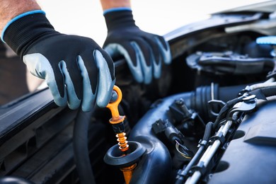 Photo of Worker checking motor oil level in car with dipstick, closeup