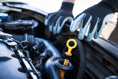Photo of Worker checking motor oil level in car with dipstick, closeup