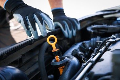 Photo of Worker checking motor oil level in car with dipstick, closeup