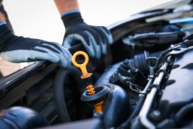 Photo of Worker checking motor oil level in car with dipstick, closeup