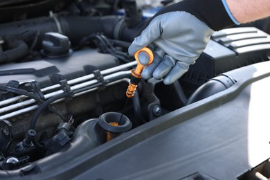Photo of Worker checking motor oil level in car with dipstick, closeup