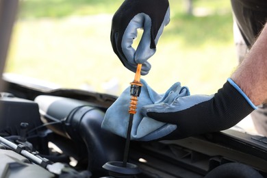 Photo of Worker checking motor oil level in car with dipstick, closeup
