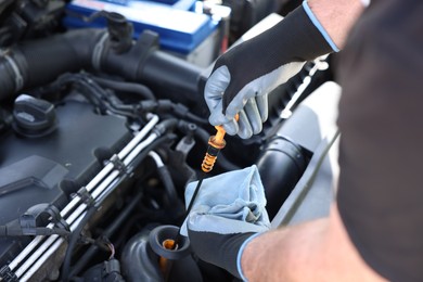Photo of Worker checking motor oil level in car with dipstick, closeup