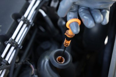 Photo of Worker checking motor oil level in car with dipstick, closeup