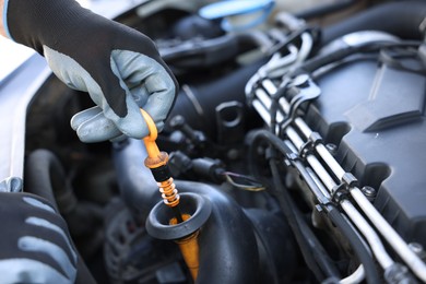 Photo of Worker checking motor oil level in car with dipstick, closeup