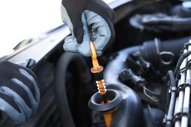 Photo of Worker checking motor oil level in car with dipstick, closeup