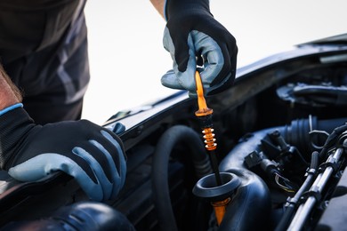 Photo of Worker checking motor oil level in car with dipstick, closeup